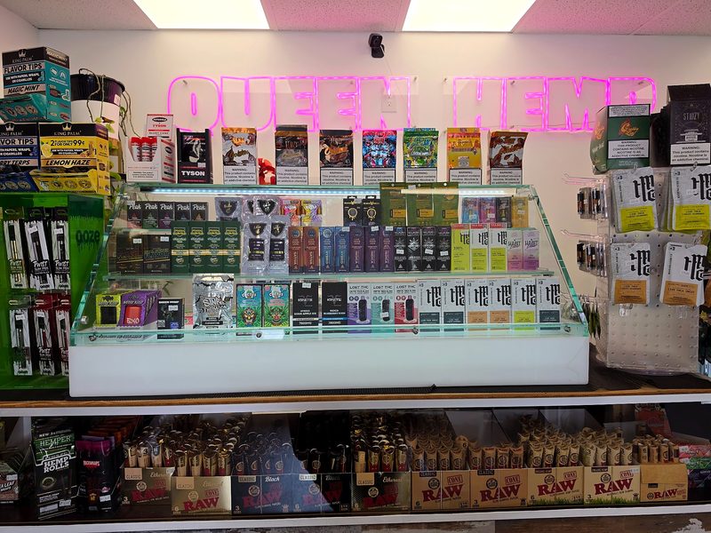 Pink Queen Hemp neon sign above a lit glass display case of vapes and hemp products